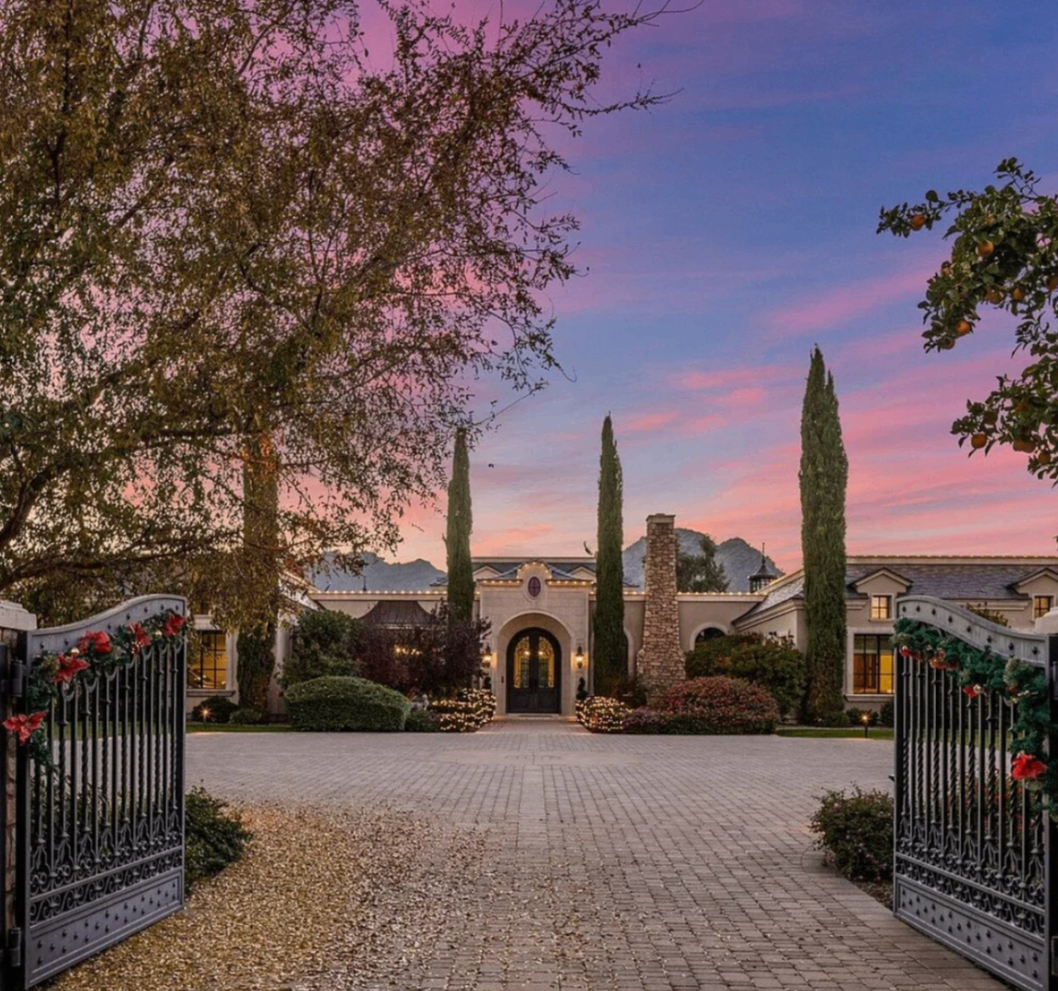 Private estate driveway framed by gates and tall cypress trees at sunset.